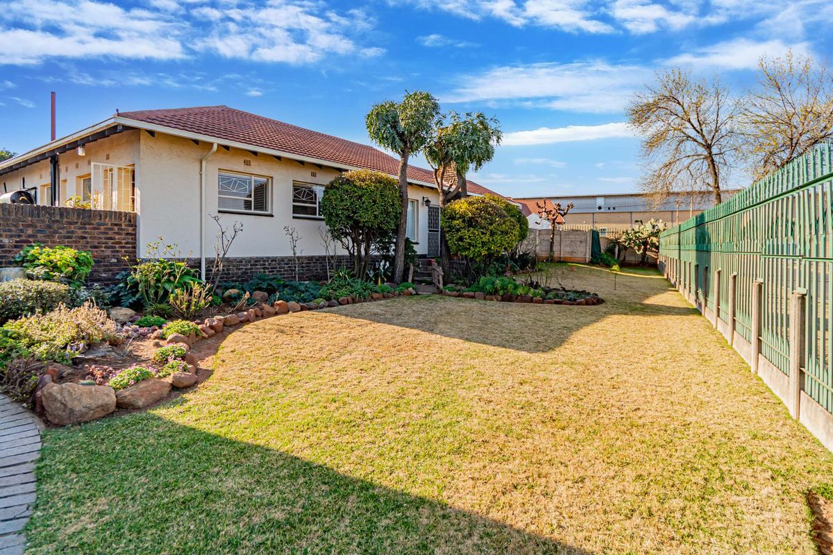 A well-maintained rear garden featuring a paved walkway, established garden beds, and secure perimeter fencing surrounding the property.