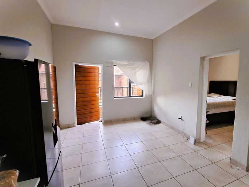 An open-plan living area featuring neutral tiled flooring, a wooden exterior door, and a window, providing a blank canvas for interior design.