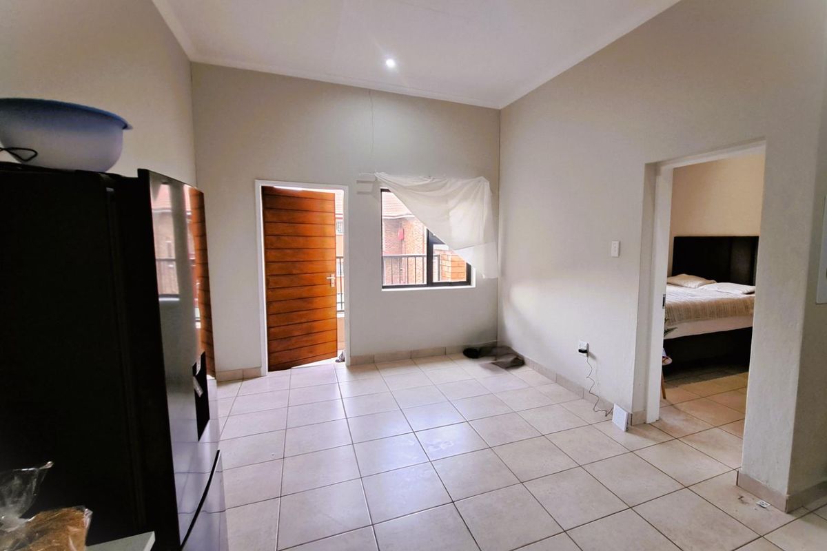 An open-plan living area featuring neutral tiled flooring, a wooden exterior door, and a window, providing a blank canvas for interior design.