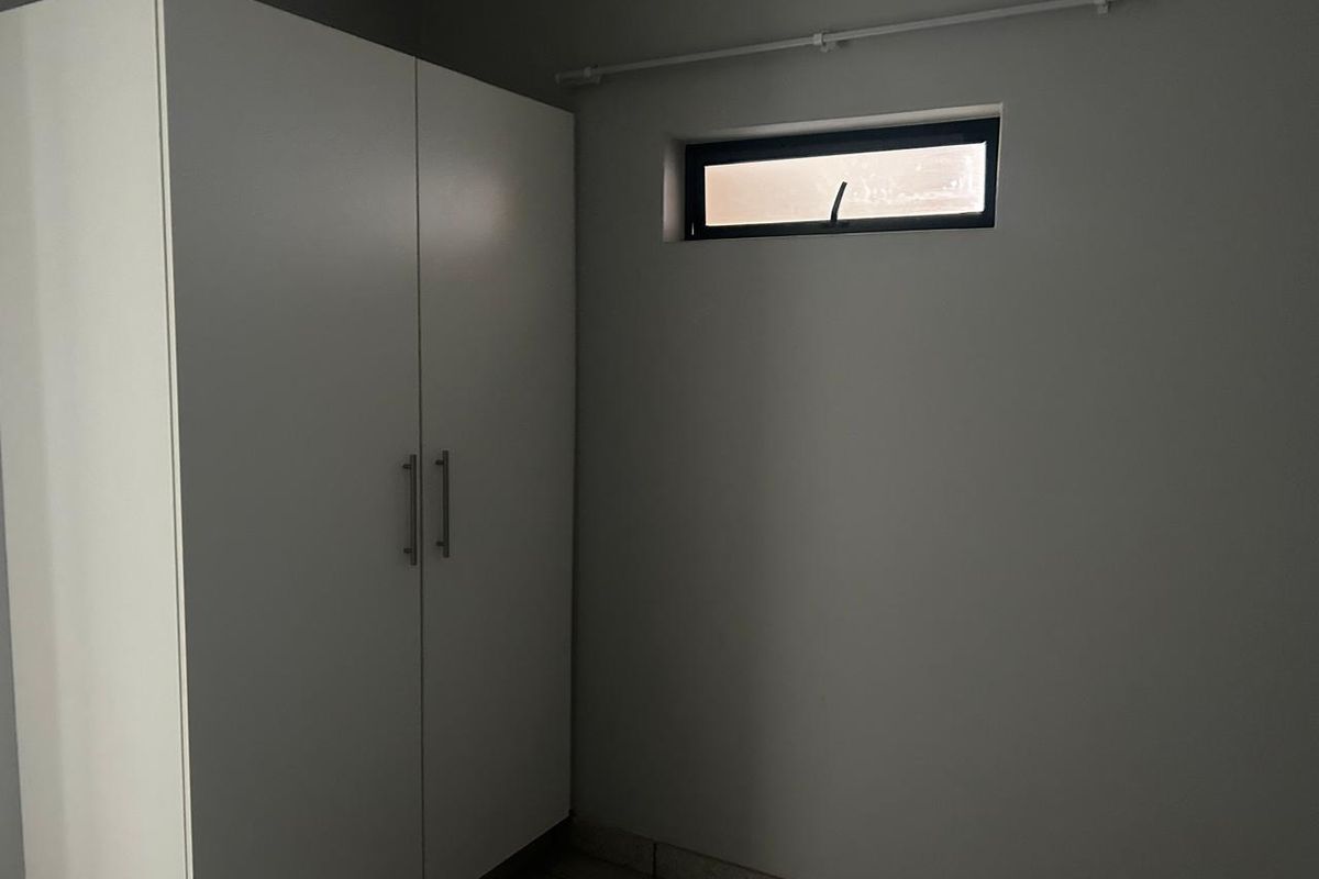 A simple room featuring a built-in white wardrobe, tiled flooring, and a small horizontal window with a curtain rod.