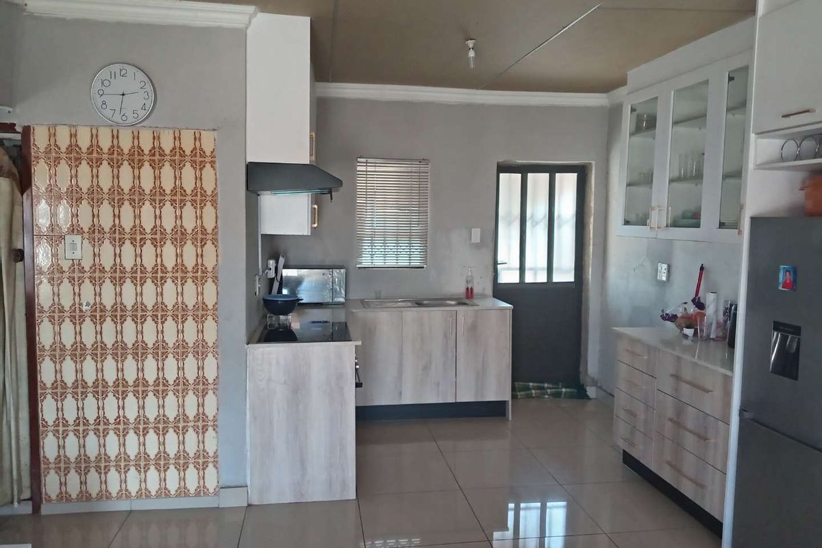 A functional kitchen featuring light wood-finish cabinetry, tiled flooring, and integrated appliances, with potential for cosmetic updates to the ceiling and wall finishes.