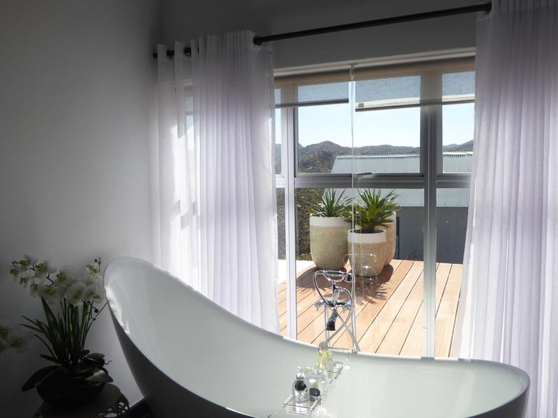 A modern bathroom featuring a sleek freestanding bathtub and large sliding glass doors that open onto a wooden deck with scenic views.