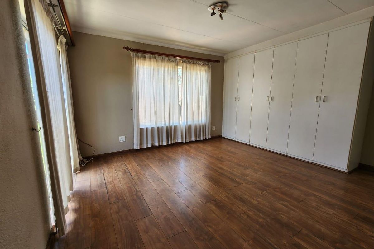 A spacious bedroom featuring wood-look laminate flooring, extensive built-in cabinetry, and large windows with natural light.