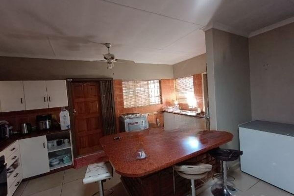 A dated kitchen featuring built-in cabinetry, a large stone-topped breakfast bar, and tiled flooring, offering potential for a modern renovation.