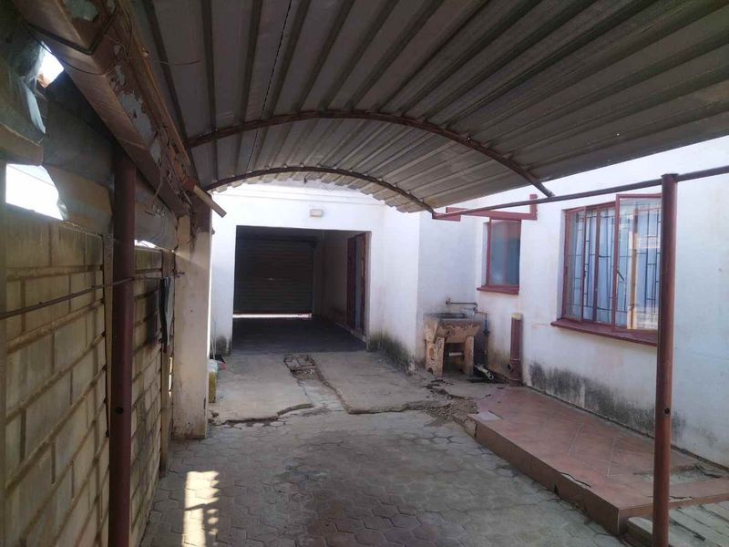 Covered outdoor patio area featuring concrete paving, an external utility sink, and metal roofing, requiring maintenance and structural repairs.