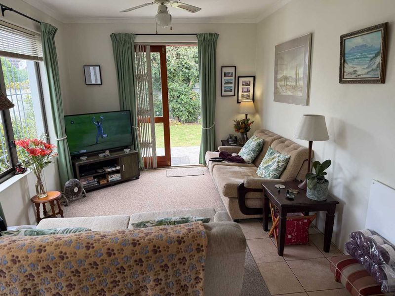 A comfortable living room featuring a ceiling fan, tiled and carpeted flooring, and a sliding glass door providing direct access to the garden.