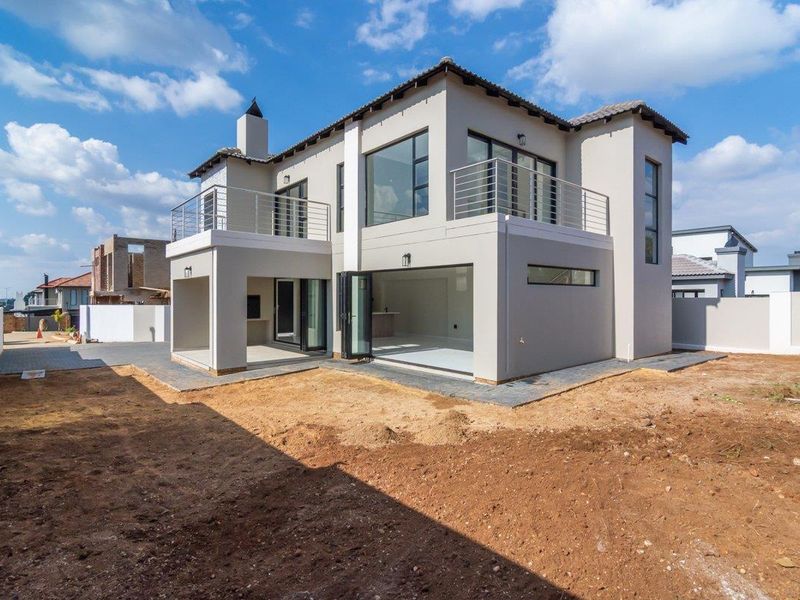 Rear view of a modern double-story house featuring a covered patio with built-in braai, upper-level balconies, and large bi-fold doors opening to the garden.