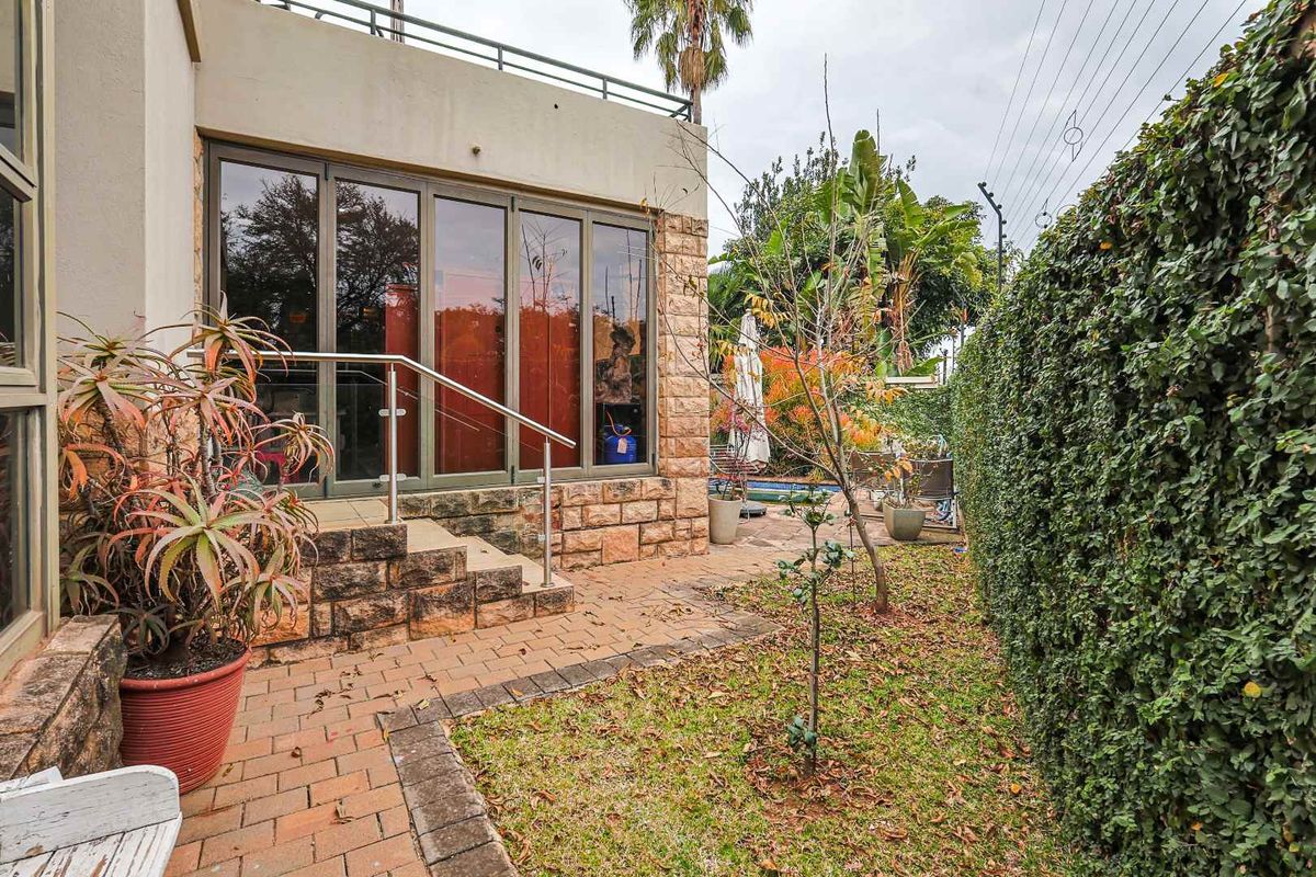 Rear garden area featuring a paved patio, stone-clad exterior wall, and access to the interior via large glass sliding doors.