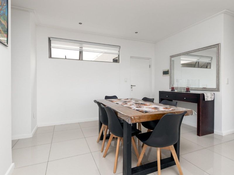 A bright and neutral dining room featuring large format floor tiles, recessed lighting, and a clean, minimalist aesthetic suitable for various interior styles.