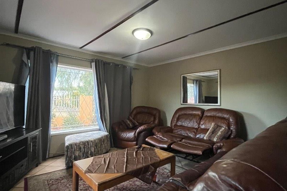 A comfortable living room featuring tiled flooring, ceiling beams, and a large window with security bars, providing a functional and well-lit space.