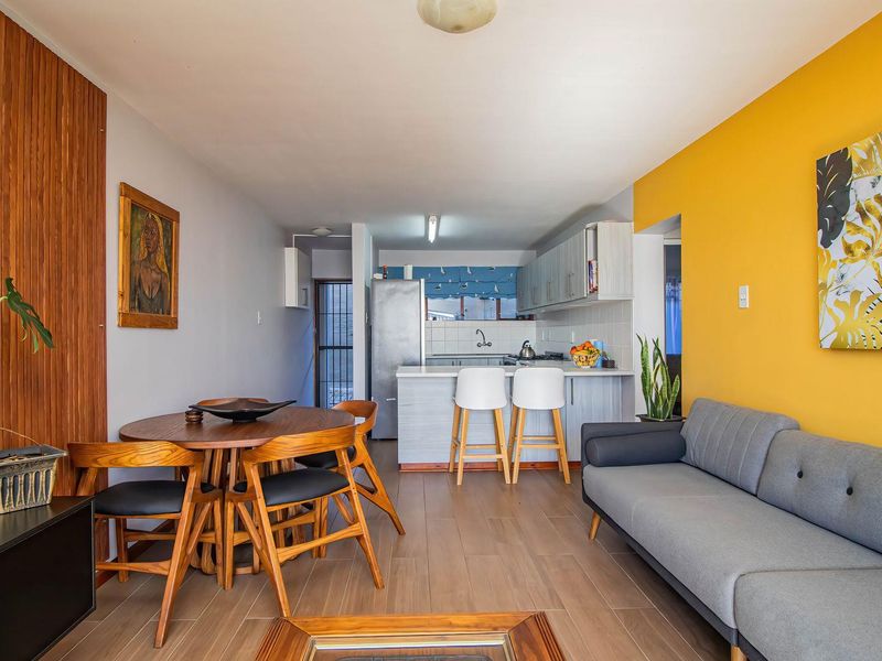 Open-plan living and dining area featuring a functional kitchen with cabinetry, tiled flooring, and a vibrant yellow accent wall.