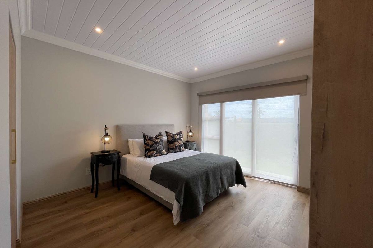 A well-maintained bedroom featuring wood-look flooring, a tongue-and-groove ceiling with recessed lighting, and large sliding glass doors with integrated roller blinds.