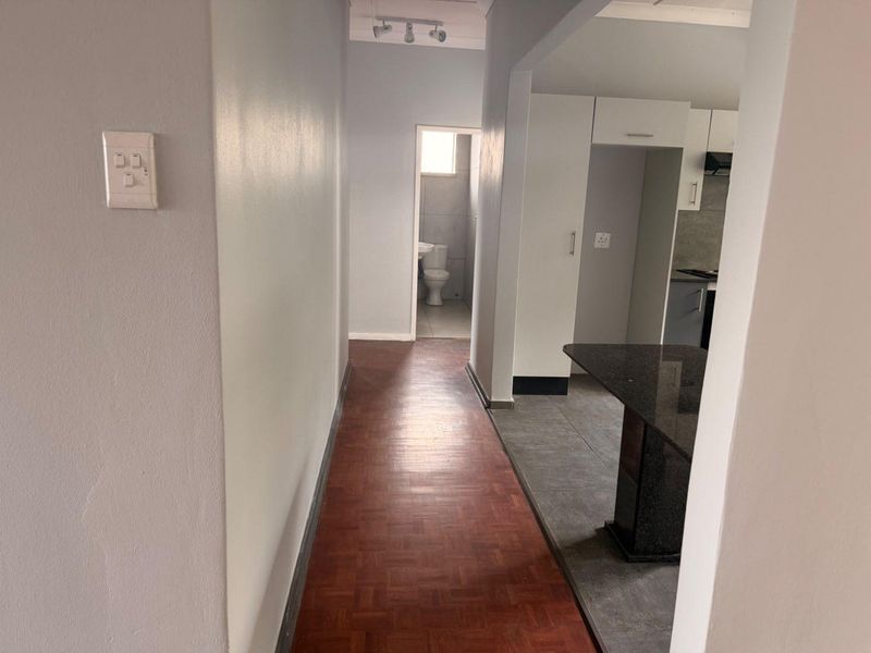 A bright hallway featuring parquet flooring, leading towards a modern kitchen area with granite breakfast bar and access to a bathroom.