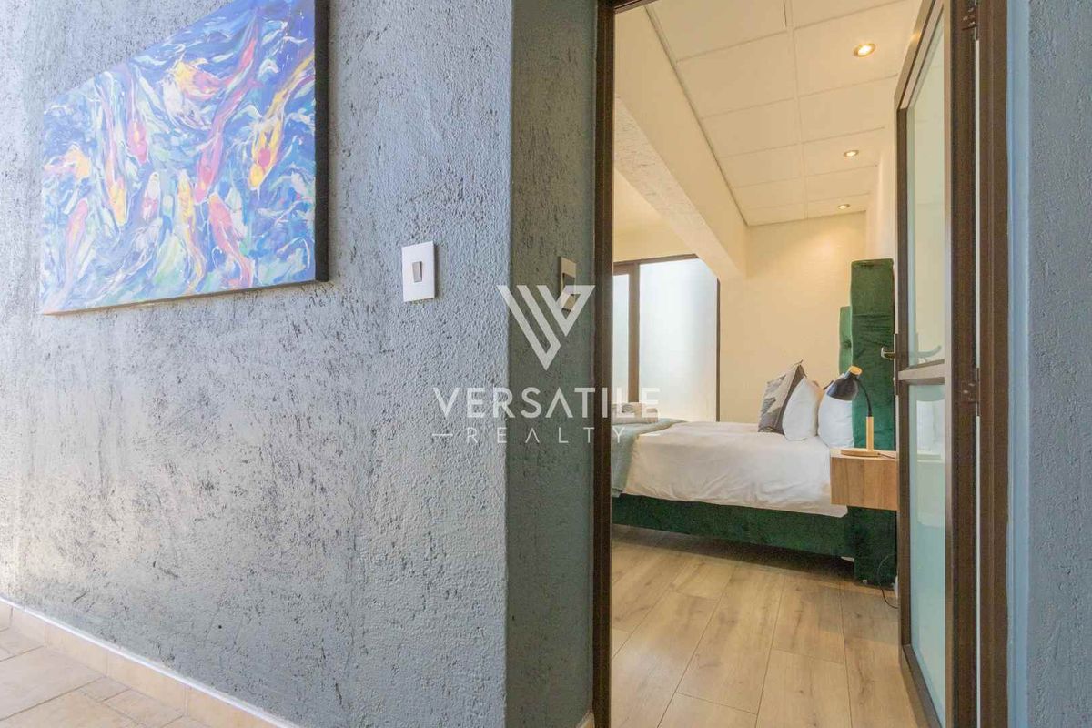 A view through a doorway into a bedroom featuring modern laminate flooring, recessed ceiling lights, and a textured wall finish in the foreground.