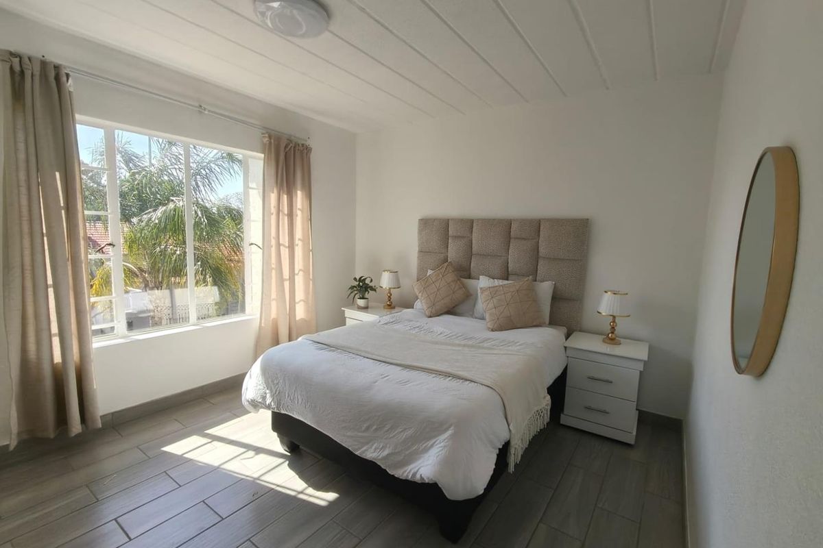 A bright and well-maintained bedroom featuring large windows, neutral tiled flooring, and a clean, modern aesthetic.
