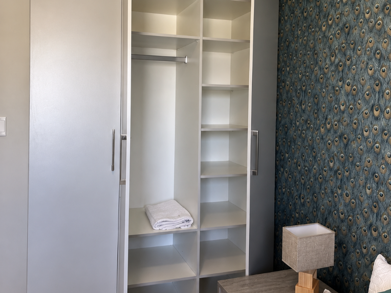 A bedroom featuring a modern built-in wardrobe with integrated shelving and hanging space, complemented by a decorative feature wall with patterned wallpaper.