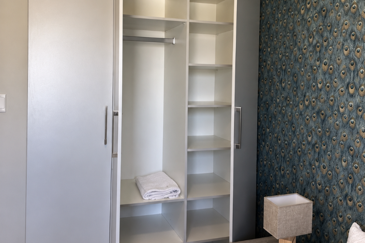 A bedroom featuring a modern built-in wardrobe with integrated shelving and hanging space, complemented by a decorative feature wall with patterned wallpaper.