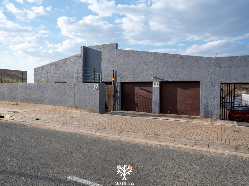 Front exterior view of a property featuring a double garage, secure boundary wall with electric fencing, and a paved driveway.