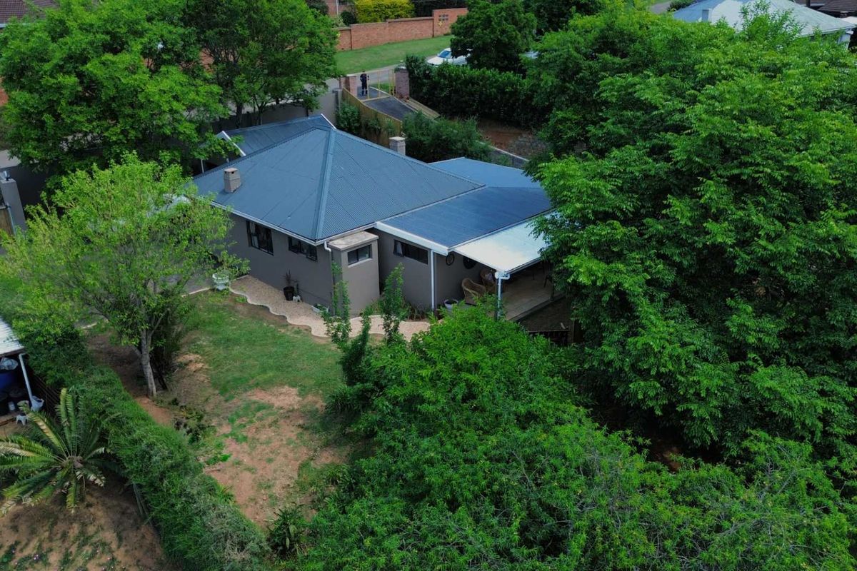 Aerial view of a residential property featuring a metal roof, a covered patio area, and a spacious garden surrounded by mature trees.