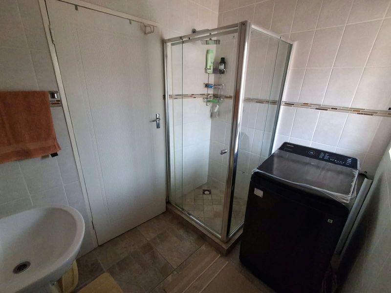 A functional bathroom featuring a corner shower enclosure, pedestal basin, and neutral ceramic wall tiling.