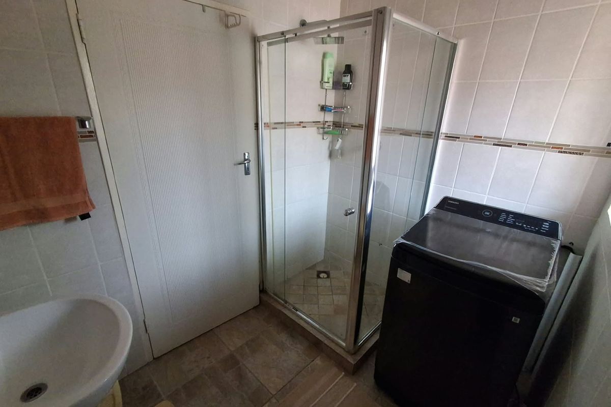A functional bathroom featuring a corner shower enclosure, pedestal basin, and neutral ceramic wall tiling.
