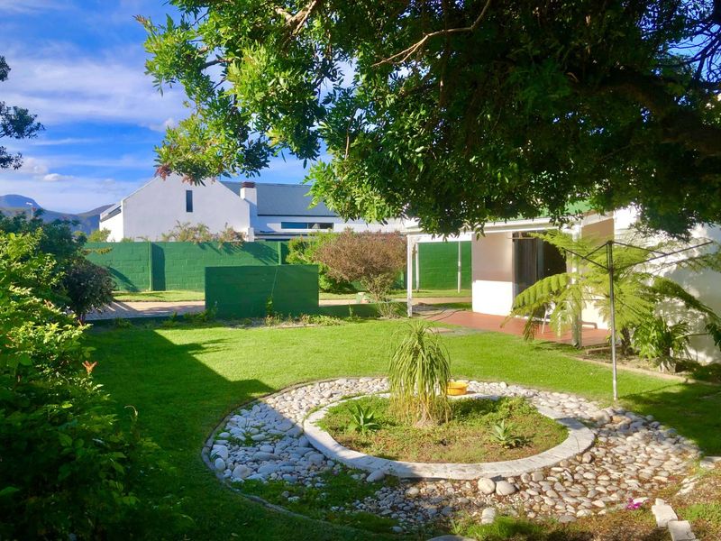A well-maintained rear garden featuring a central stone-bordered garden bed, lush lawn, and a covered patio area.