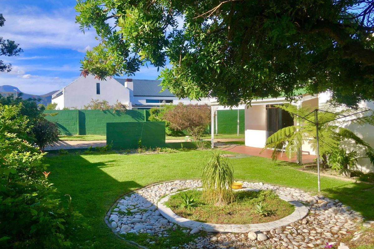 A well-maintained rear garden featuring a central stone-bordered garden bed, lush lawn, and a covered patio area.