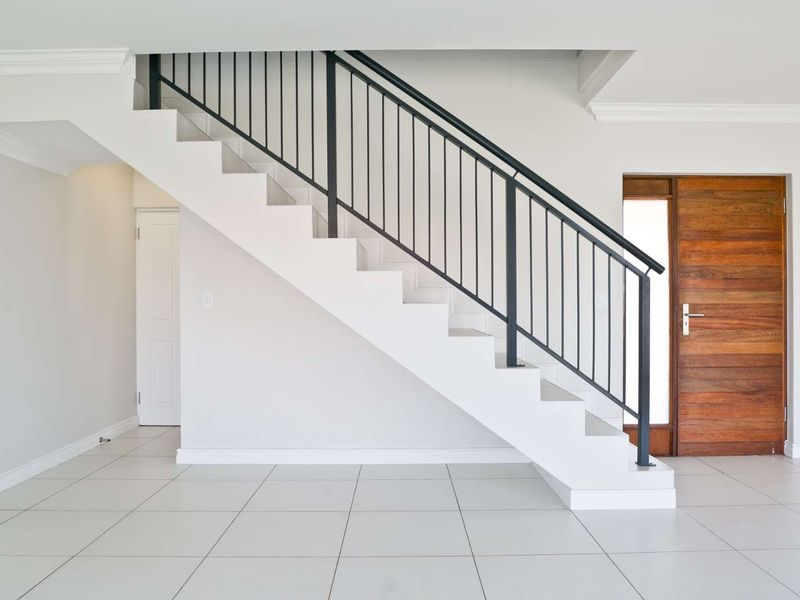 Bright and spacious entrance hall featuring a modern staircase with a metal balustrade, tiled flooring, and a solid timber front door.