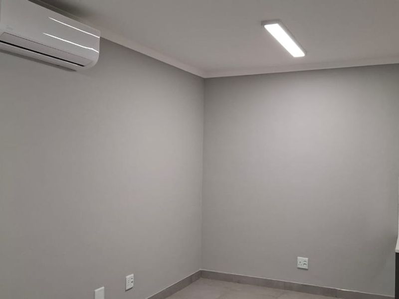 A clean, modern office space featuring neutral grey walls, tiled flooring, a wall-mounted air conditioner, and a convenient built-in vanity with a vessel sink.