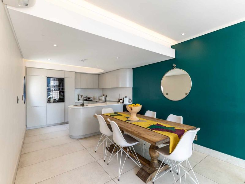 Modern open-plan kitchen and dining area featuring sleek built-in cabinetry, integrated appliances, tiled flooring, and recessed lighting in a well-maintained apartment setting.