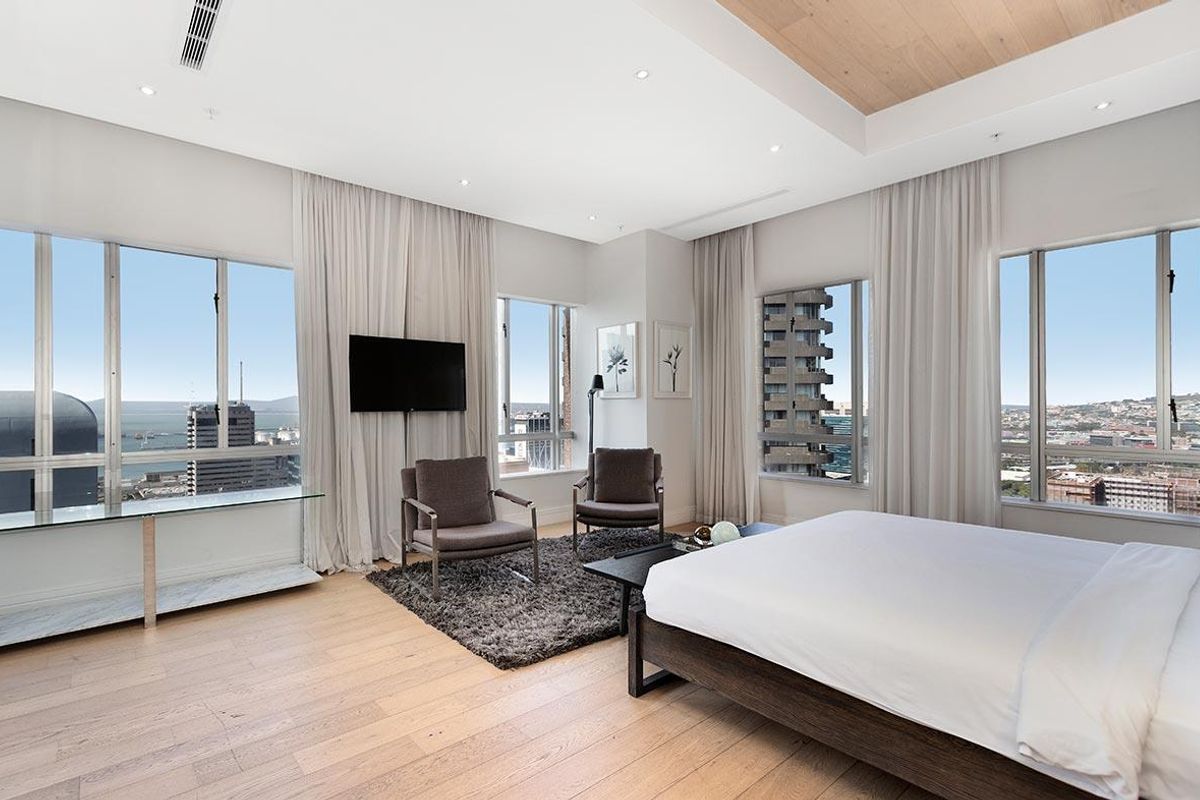 Spacious bedroom featuring light oak hardwood flooring, recessed ceiling lighting, and expansive windows offering panoramic city and coastal views.