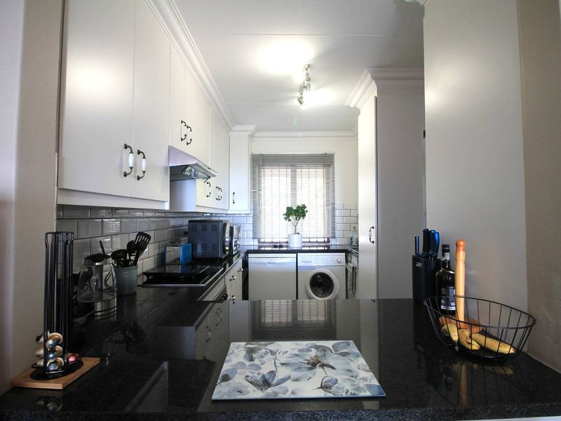 A well-maintained kitchen featuring dark granite countertops, white cabinetry, subway tile backsplash, and integrated laundry facilities.