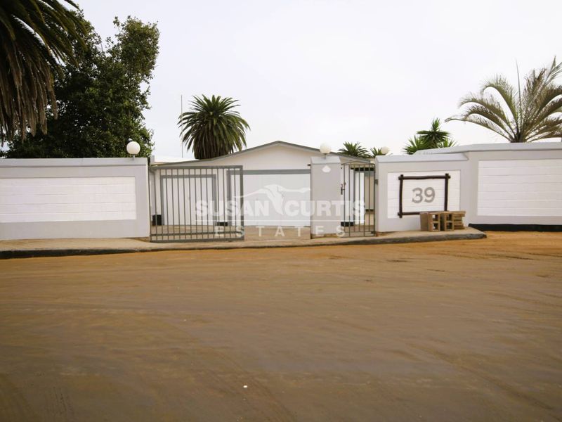 Front exterior view of the property featuring a secure boundary wall, metal gate, and pillar lighting.