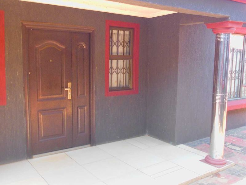 Front entrance porch featuring a tiled floor, security door, and metal support column with decorative red trim accents.