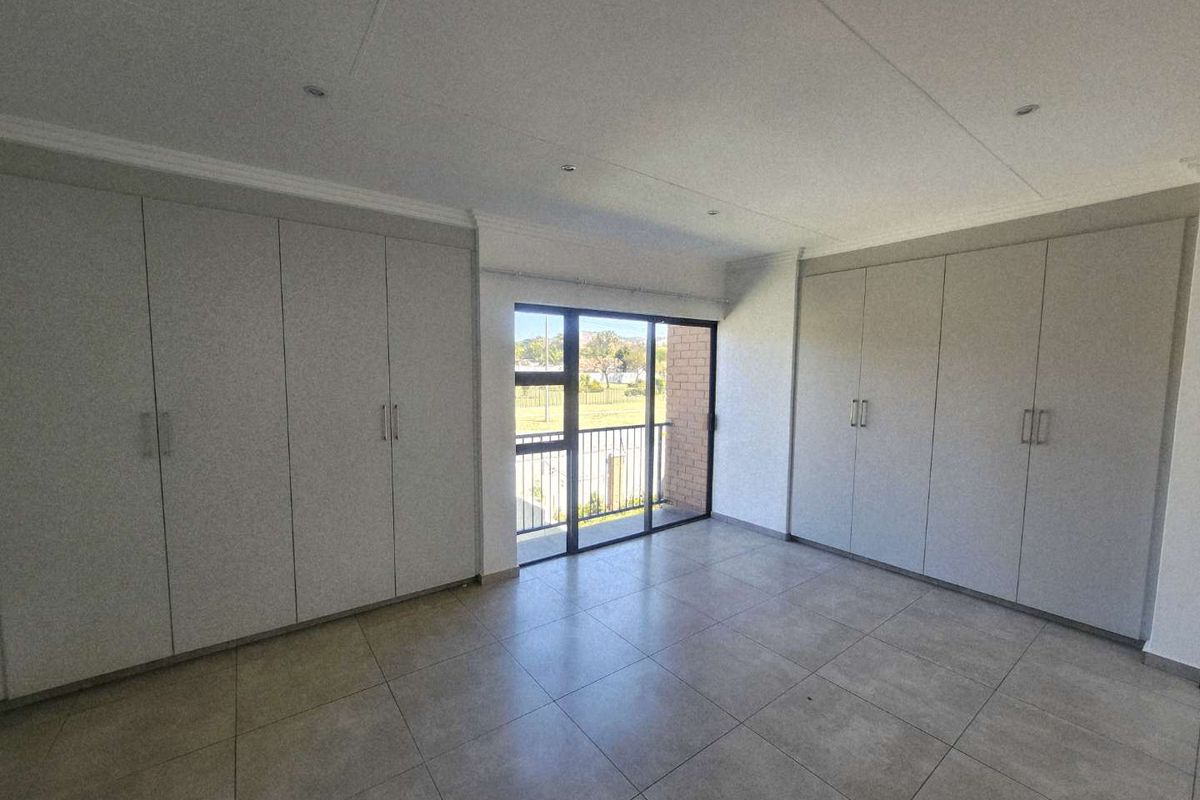 Spacious bedroom featuring extensive built-in cupboards, neutral tiled flooring, and a sliding glass door providing access to a balcony.