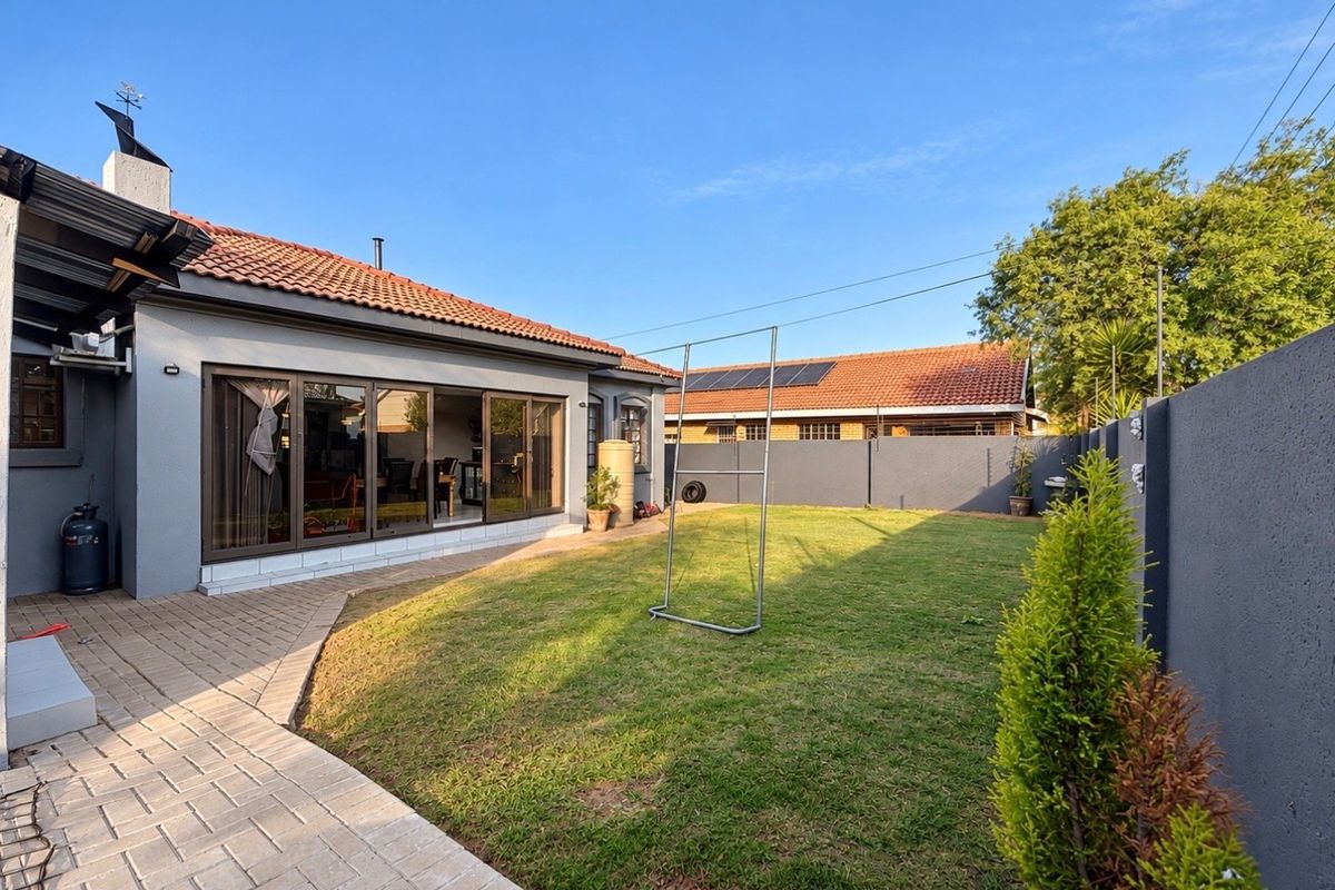 A well-maintained rear garden featuring a paved walkway, a neat lawn, and a modern exterior facade with large sliding glass doors.