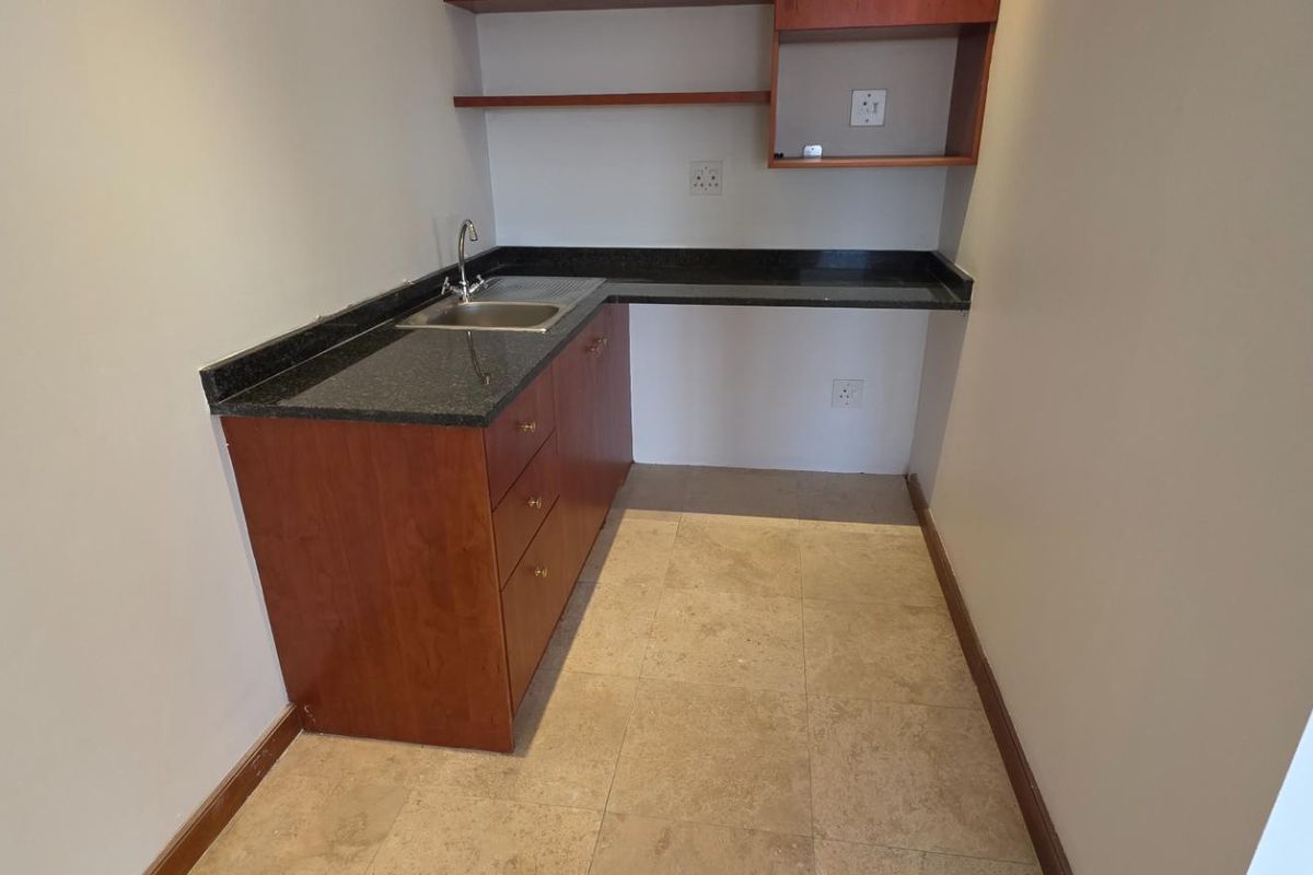 A compact office kitchenette featuring granite countertops, built-in wooden cabinetry, a stainless steel sink, and tiled flooring.