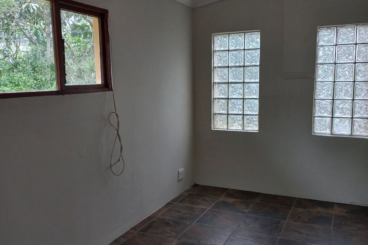 An empty bedroom featuring ceramic floor tiles, glass block windows, and an exposed ceiling beam, providing a neutral canvas for interior design.