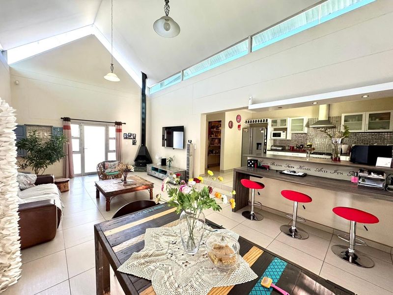 Spacious open-plan living area featuring a vaulted ceiling, clerestory windows, a modern suspended fireplace, and a functional kitchen with a breakfast bar.