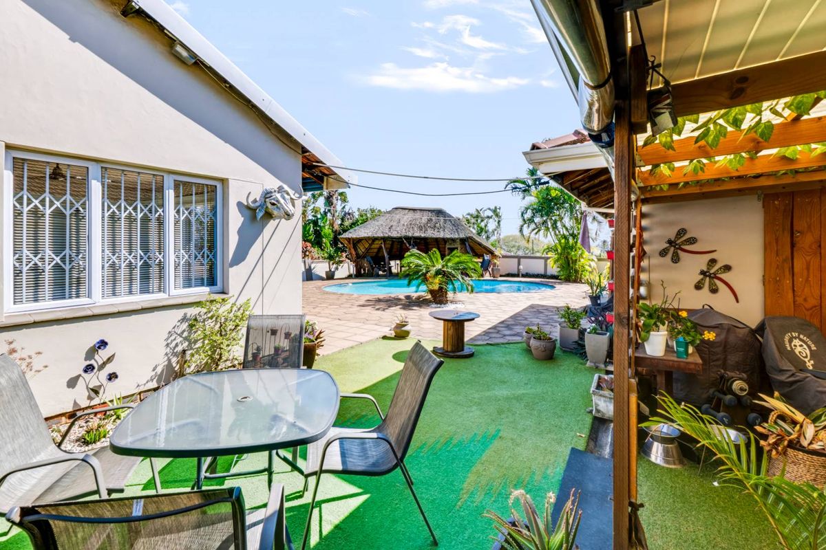 Rear outdoor entertainment area featuring a covered patio, artificial lawn, and a swimming pool with a thatched lapa in the background.