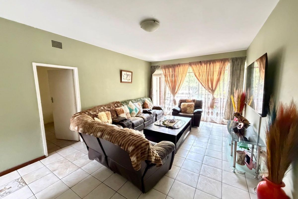 A spacious living room featuring neutral ceramic floor tiles, large windows with natural light, and access to an adjoining balcony area.