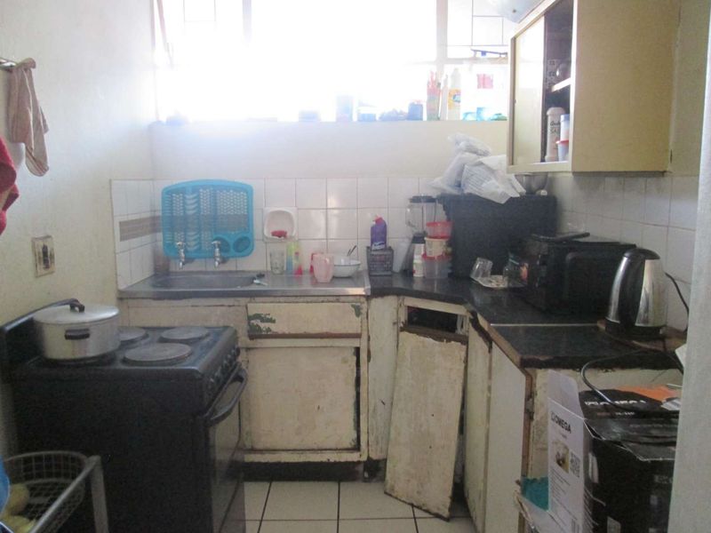 A dated kitchen featuring tiled backsplash, built-in cabinetry, and tiled flooring, currently showing significant wear and damage to the cabinet units.