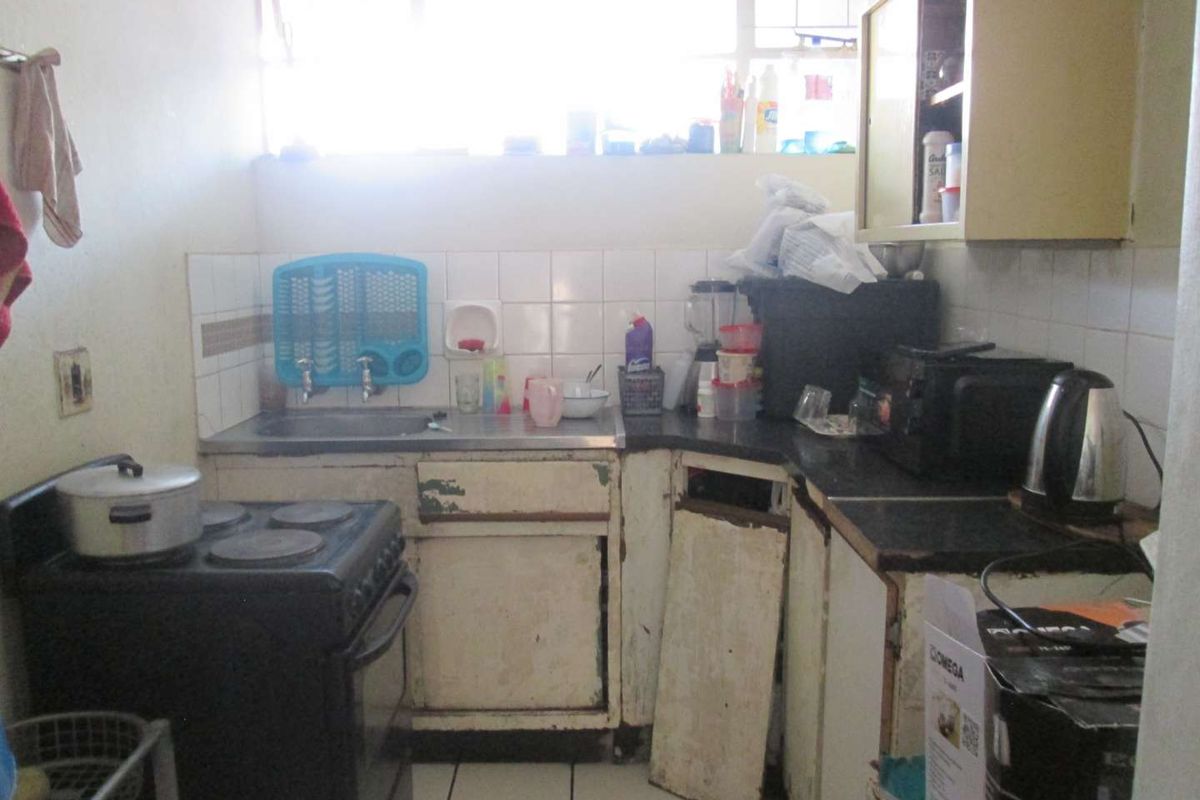 A dated kitchen featuring tiled backsplash, built-in cabinetry, and tiled flooring, currently showing significant wear and damage to the cabinet units.