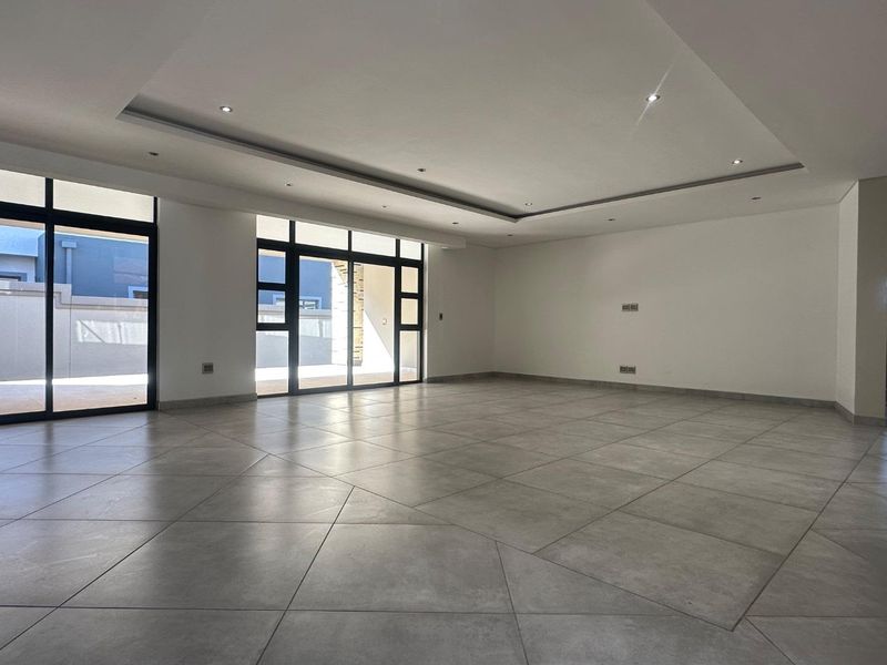 A spacious, modern, and empty living area featuring large format floor tiles, recessed ceiling lighting, and expansive aluminium sliding doors leading to the exterior.