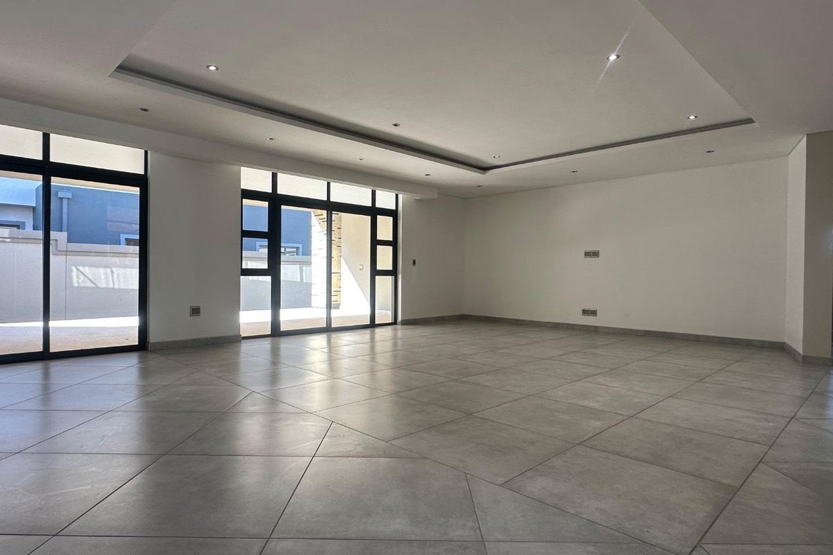 A spacious, modern, and empty living area featuring large format floor tiles, recessed ceiling lighting, and expansive aluminium sliding doors leading to the exterior.