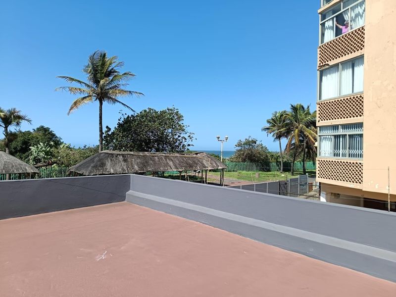 A spacious open-air balcony featuring a solid parapet wall with views overlooking the surrounding landscape and distant ocean.