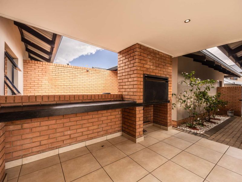 Covered patio area featuring a built-in brick braai, tiled flooring, and exposed rafters, perfect for outdoor entertaining.