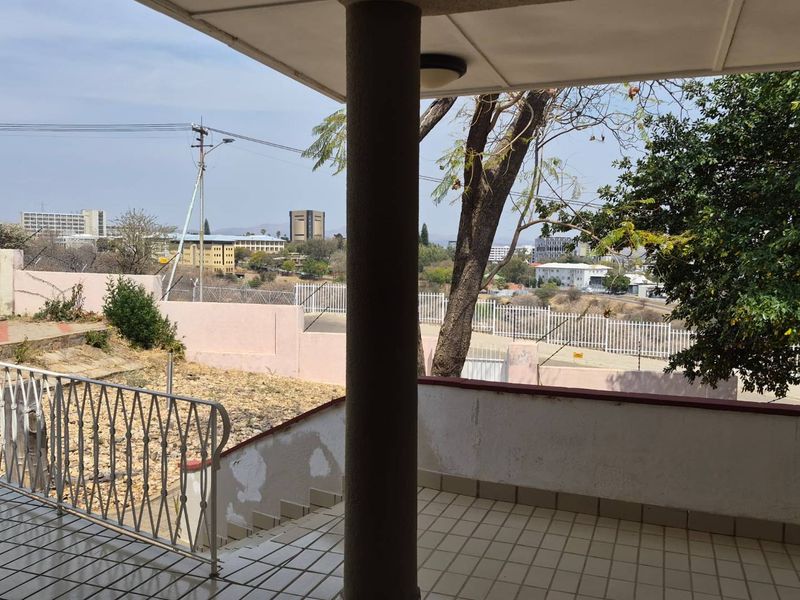 A covered outdoor patio area featuring tiled flooring, a support column, and metal railings, overlooking the surrounding neighborhood.
