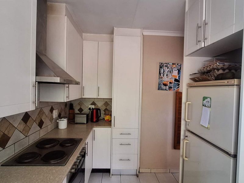 A functional kitchen featuring white cabinetry, a built-in electric hob with extractor fan, tiled backsplash, and tiled flooring.