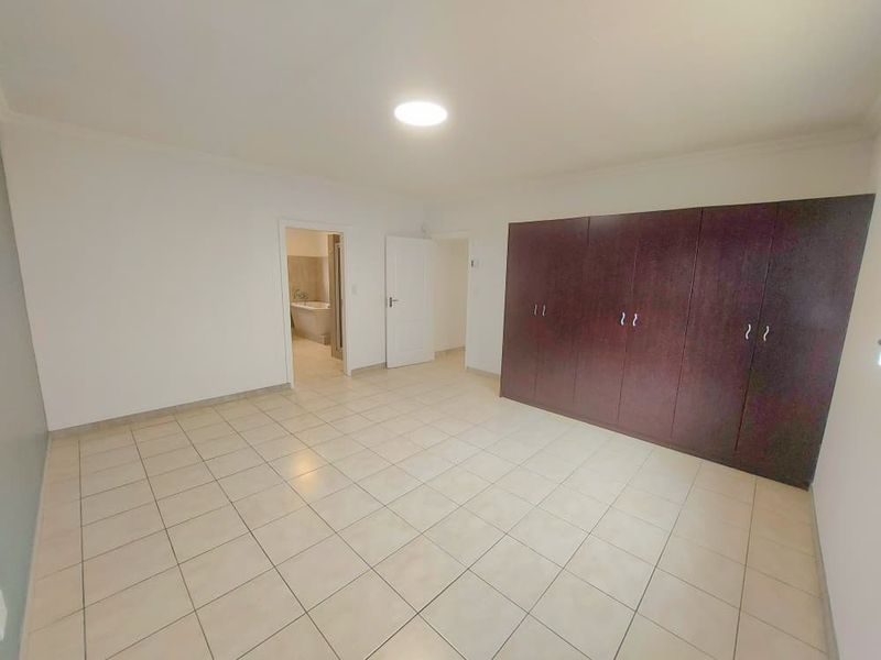 Spacious bedroom featuring neutral tiled flooring, extensive dark wood built-in cupboards, and direct access to an en-suite bathroom.